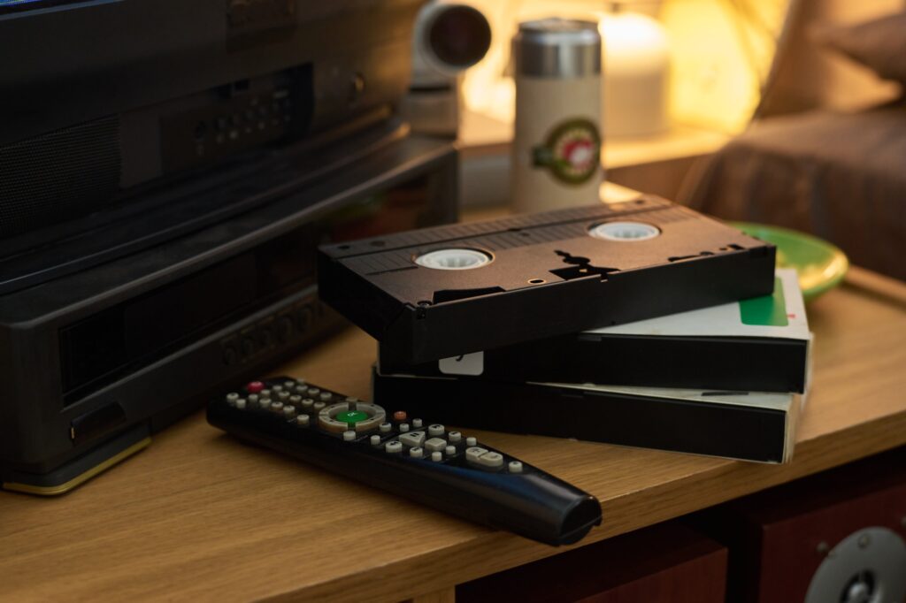 Stacking Vintage VHS Tapes Near Remote Control On Wooden Table